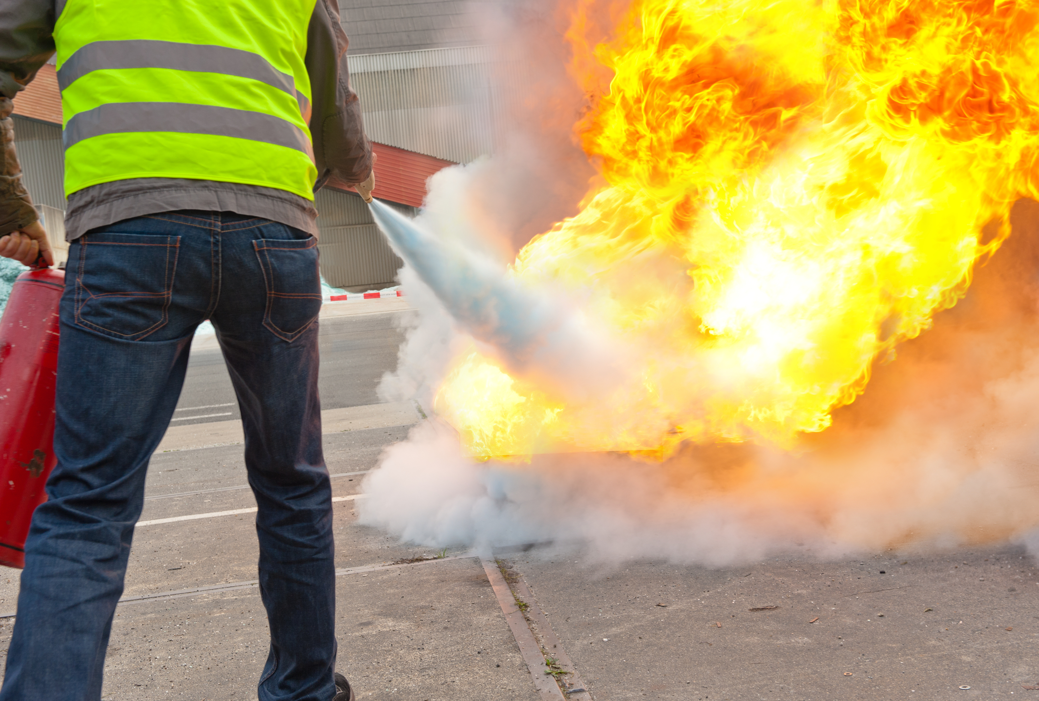 Eine Person mit Warnweste löscht ein Feuer mit einem Feuerlöscher.