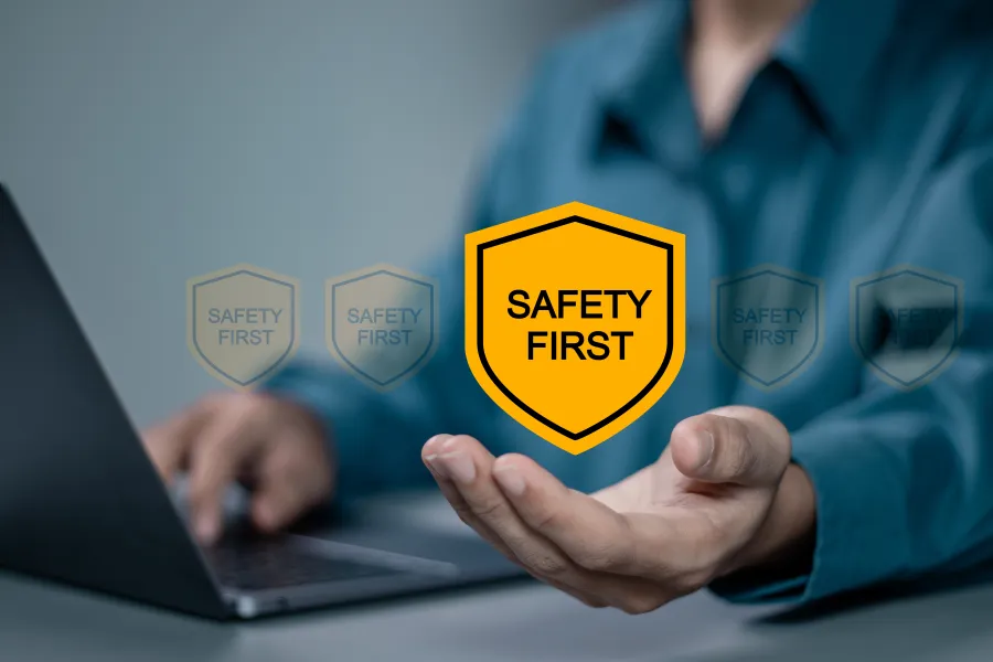 Eine Person sitzt am Laptop und schwebend über seiner linken Hand sieht man ein gelbes Schild auf dem Safety First steht. 