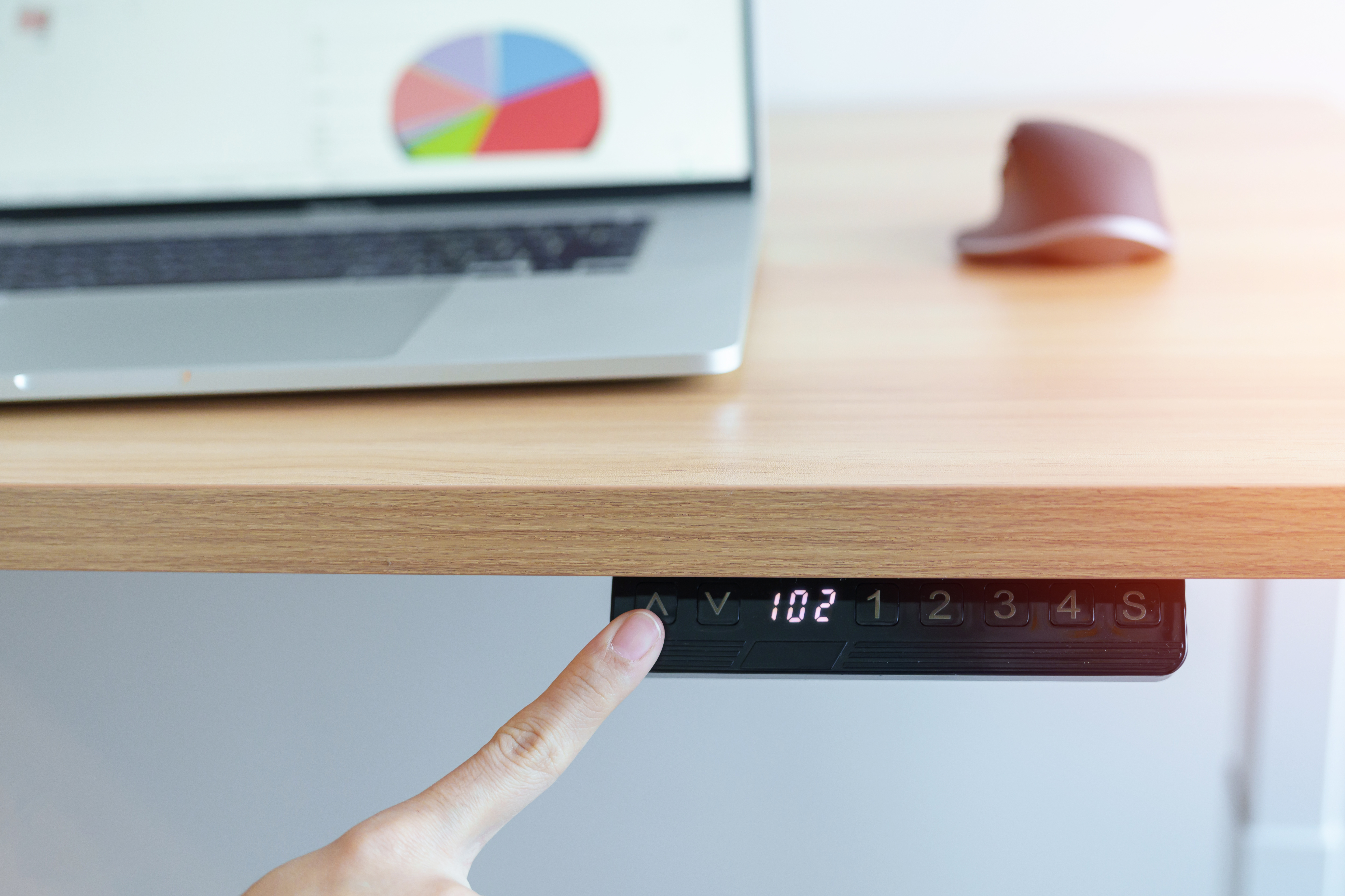 Ein höhenverstellbarer Schreibtisch und ein Finger, der diesen bedient.