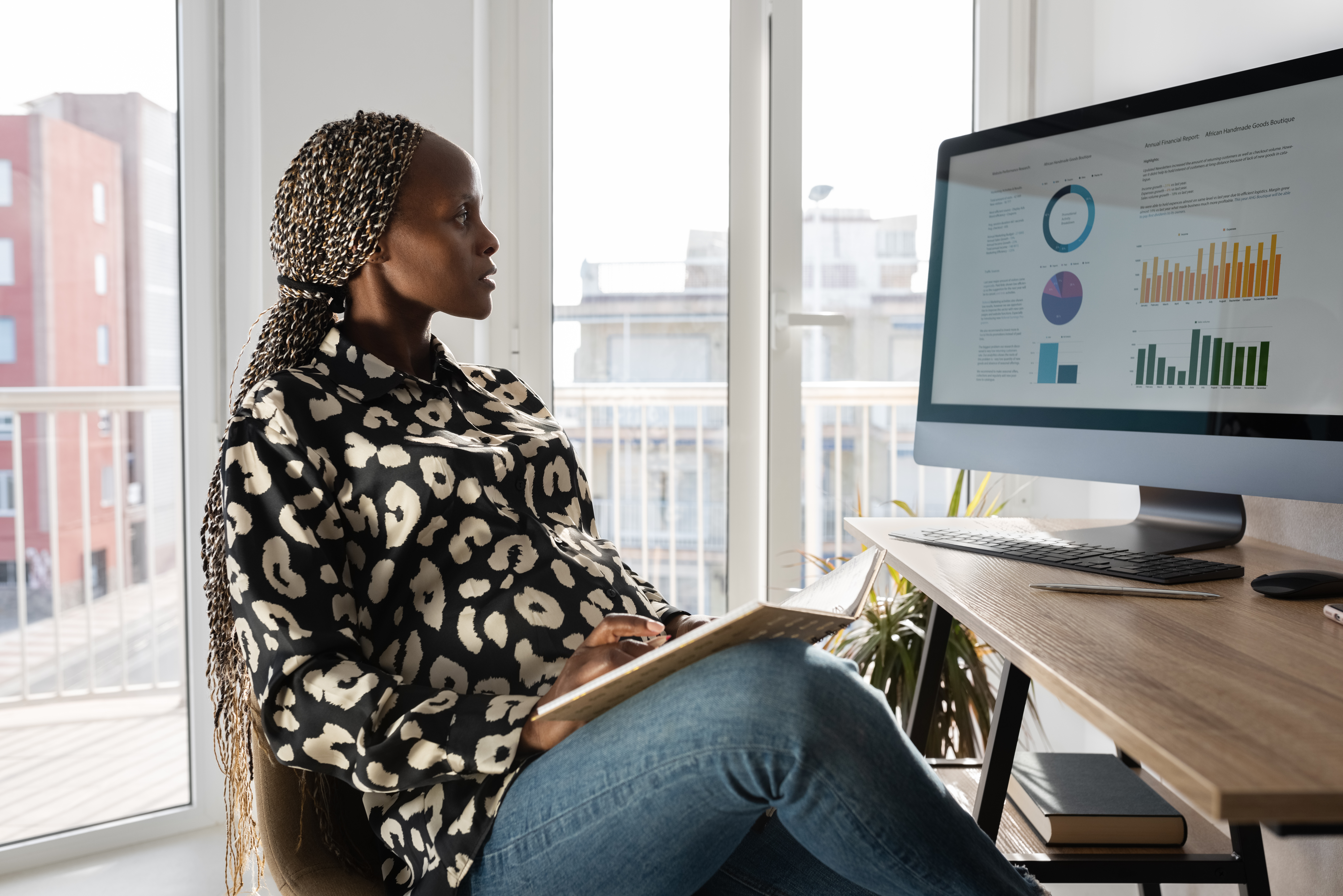 Eine Frau sitzt an einem Schreibtisch und schaut sich Diagramme auf ihrem Computer Bildschirm an.