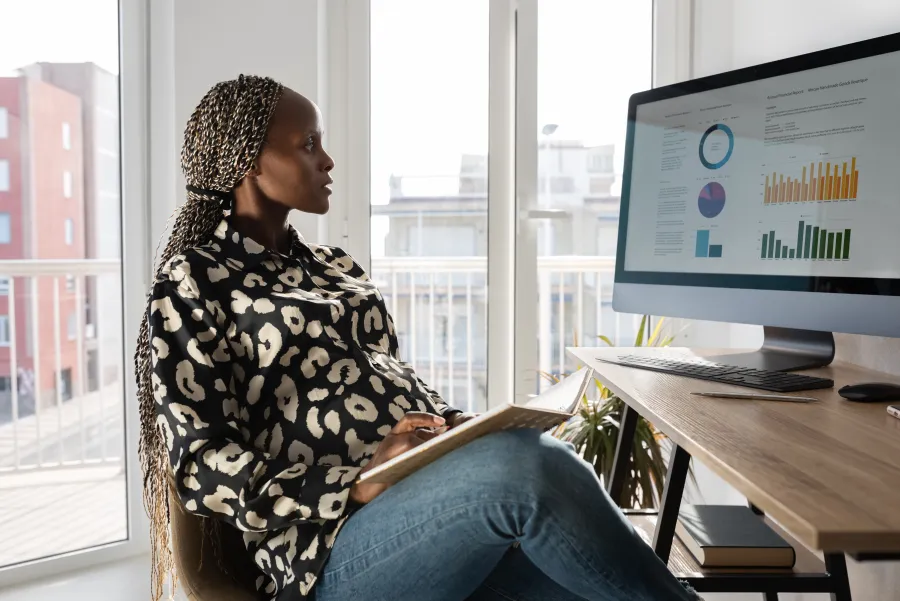 Eine Frau sitzt an einem Schreibtisch und schaut sich Diagramme auf ihrem Computer Bildschirm an.