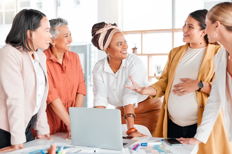 Fünf Frauen stehen um einen Laptop und unterhalten sich lachend. 