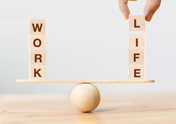 Holzklötze mit den Worten Work und Life balancieren auf einem Brett und einer Kugel